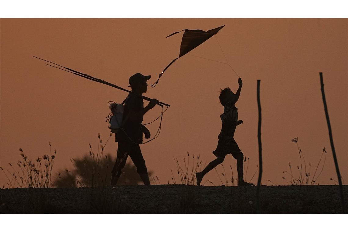 Ein Junge (r) lässt einen Drachen steigen, während er mit seinem Vater nach dem Fischen am Stadtrand von Phnom Penh nach Hause geht.