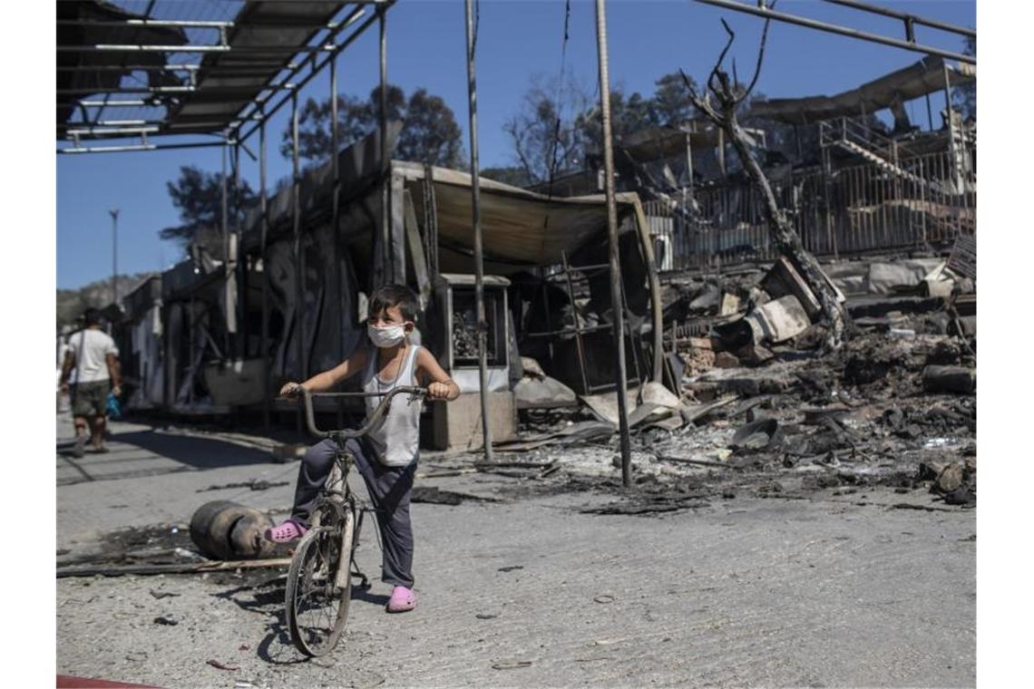 Ein Junge steht vor verbrannten Trümmern in Moria. Dem Großbrand vorangegangen waren Unruhen unter den Migranten, weil das Lager nach einem ersten Corona-Fall unter Quarantäne gestellt worden war. Foto: Petros Giannakouris/AP/dpa