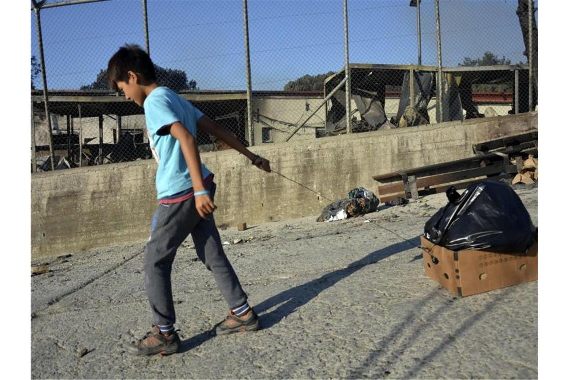 Ein Junge zieht nach dem Brand im Flüchtlingslager einen Karton mit einer Plastiktüte hinter sich her. Foto: Panagiotis Balaskas/AP/dpa