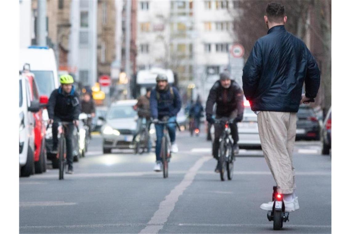 Ein junger Mann fährt auf einem E-Scooter eine Straße in Stuttgart entlang, während drei Fahrradfahrer ihm entgegenkommen. Foto: Gregor Bauernfeind/dpa/Archivbild