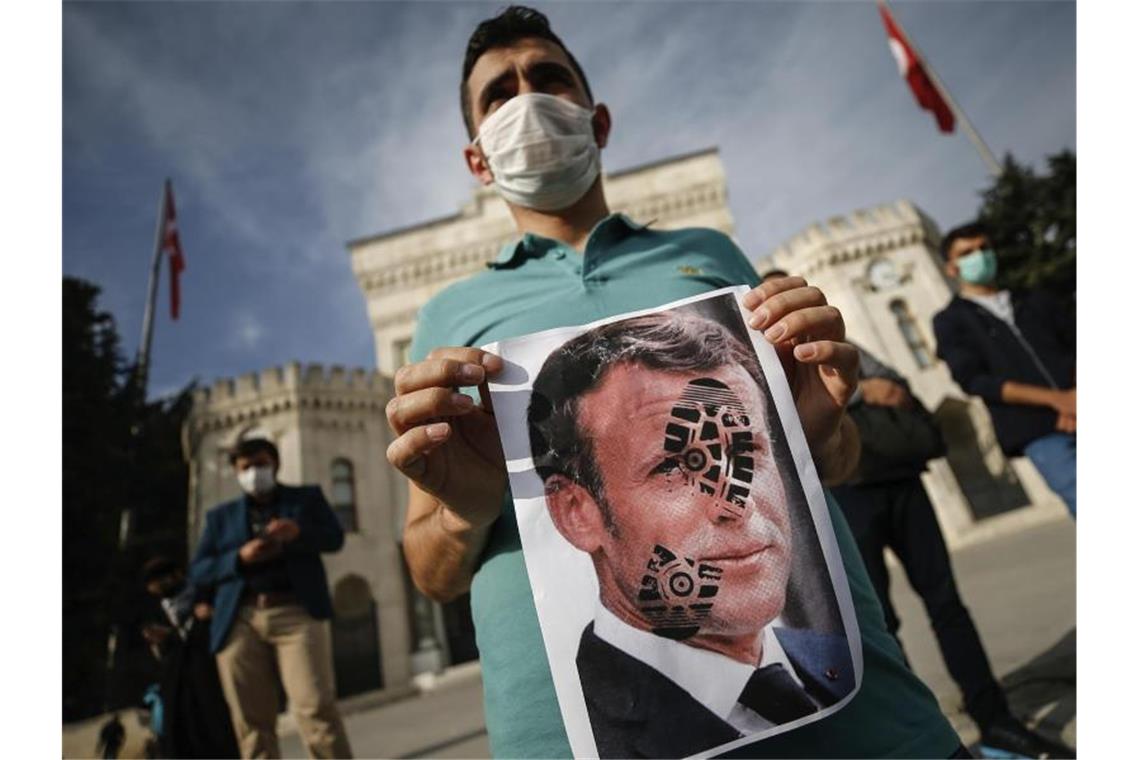 Ein junger Mann hält ein mit einem Schuhabdruck versehenes Foto von Emmanuel Macron, Präsident von Frankreich, in die Kamera. Recep Tayyip Erdogan, Präsident der Türkei, griff Macron ein zweites Mal verbal an und warf ihm Islamfeindlichkeit vor. Foto: Emrah Gurel/AP/dpa