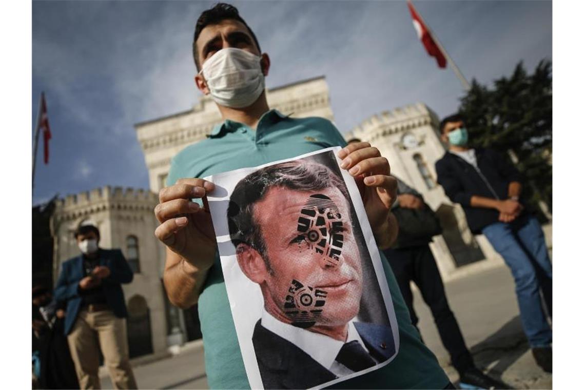 Ein junger Mann hält in Istanbul ein mit einem Schuhabdruck versehenes Foto von Emmanuel Macron in die Kamera. Foto: Emrah Gurel/AP/dpa
