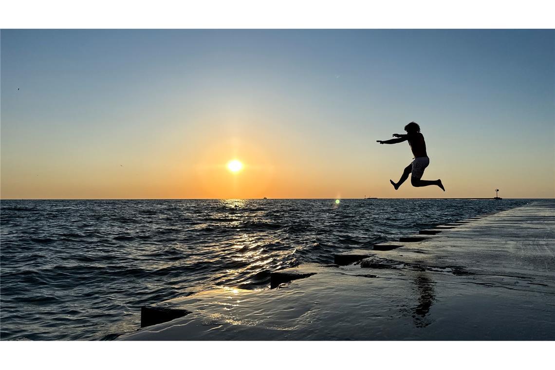 Ein junger Mann springt am frühen Morgen in Chicago von der Promenade am „Oak Street Beach“ in den Lake Michigan.