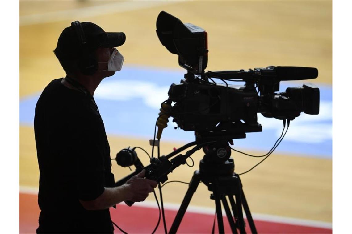 Ein Kameramann steht mit Mundschutz bei einem Basketballspiel an seiner TV-Kamera. Foto: Andreas Gebert/Reuters-Pool/dpa