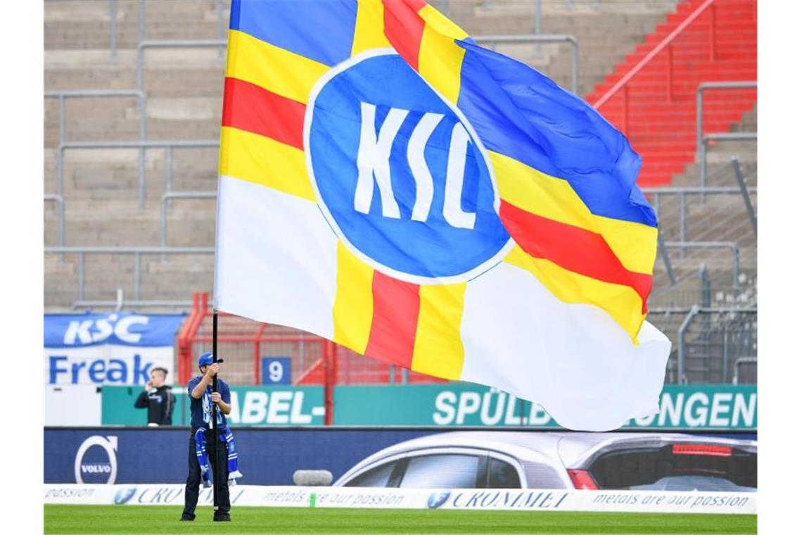 Ein Karlsruher Fan schwenkt vor leeren Zuschauerrängen eine Fahne mit der Aufschrift „KSC“. Foto: Uwe Anspach/Archivbild