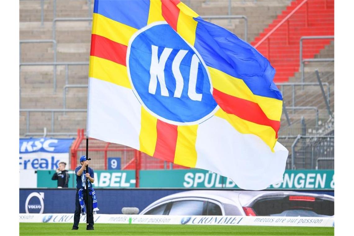 Ein Karlsruher Fan schwenkt vor Spielbeginn vor leeren Zuschauerrängen eine Fahne mit der Aufschrift "KSC". Foto: Uwe Anspach/Archiv