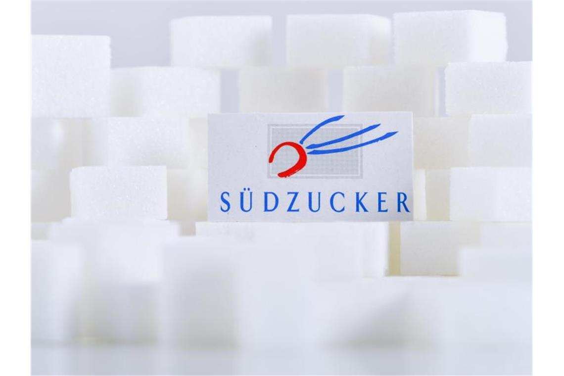 Südzucker rutscht in rote Zahlen: „Schwieriges Marktumfeld“ Ein Kartonausschnitt mit dem Schriftzug von Südzucker liegt auf Zuckerwürfeln. Foto: Uwe Anspach/dpa/Archivbild