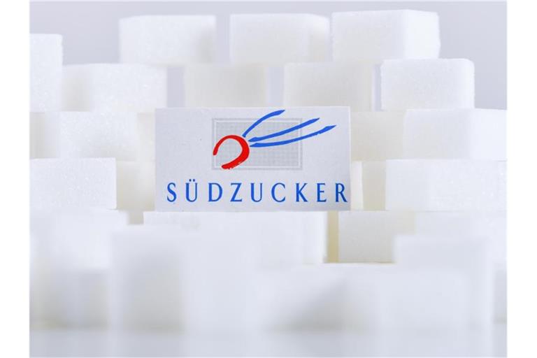 Ein Kartonausschnitt mit dem Schriftzug von Südzucker liegt auf Zuckerwürfeln. Foto: Uwe Anspach/dpa/Archivbild
