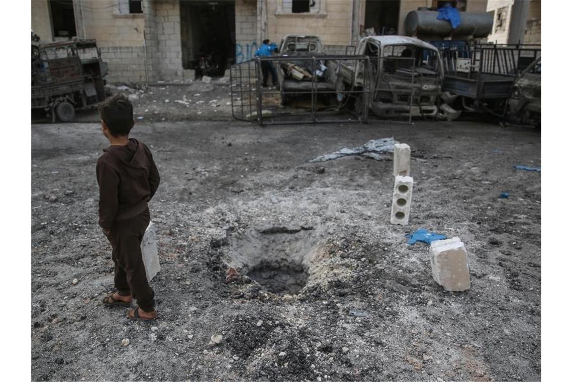 Ein Kind geht in Idlib nach einem Raketenbeschuss an einer Einschlagstelle im Boden vorbei. Foto: Anas Alkharboutli/dpa