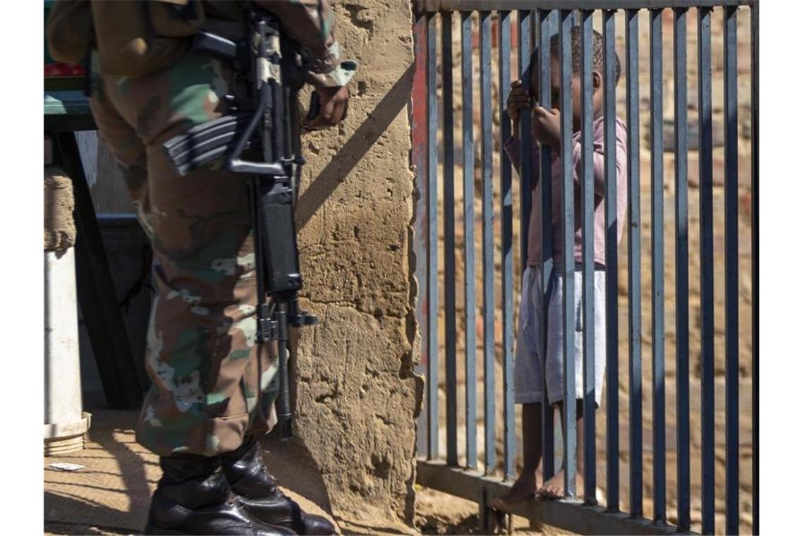 Ein Kind hält sich im südafrikanischen Johannesburg an einem Torgitter fest, hinter dem ein Mitglied der Nationalen Verteidigungskräfte steht. Foto: Themba Hadebe/AP/dpa