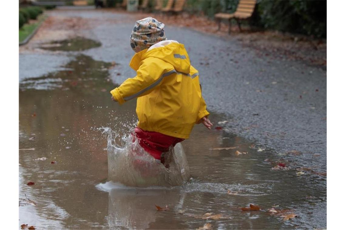 Ein Kind hüpft in eine Regenpfütze. Foto: Paul Zinken/dpa/Archivbild