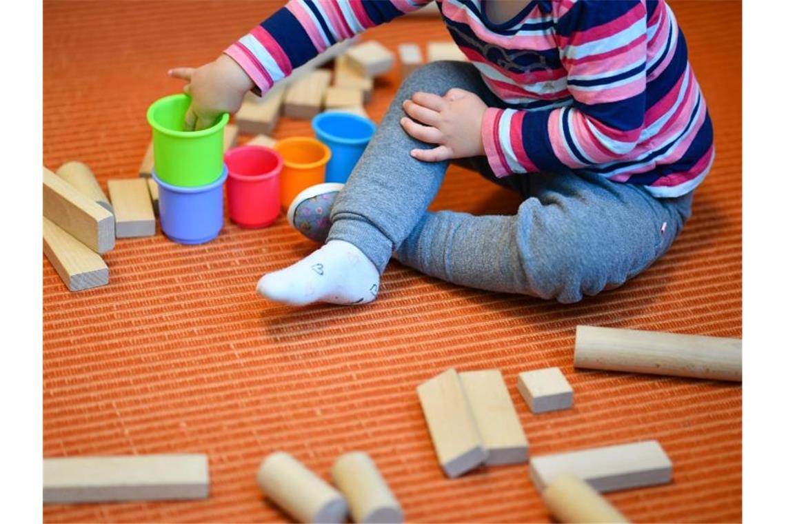 Ein Kind spielt auf dem Boden sitzend mit bunten Bechern und Bauklötzen. Foto: Uwe Anspach/Archiv