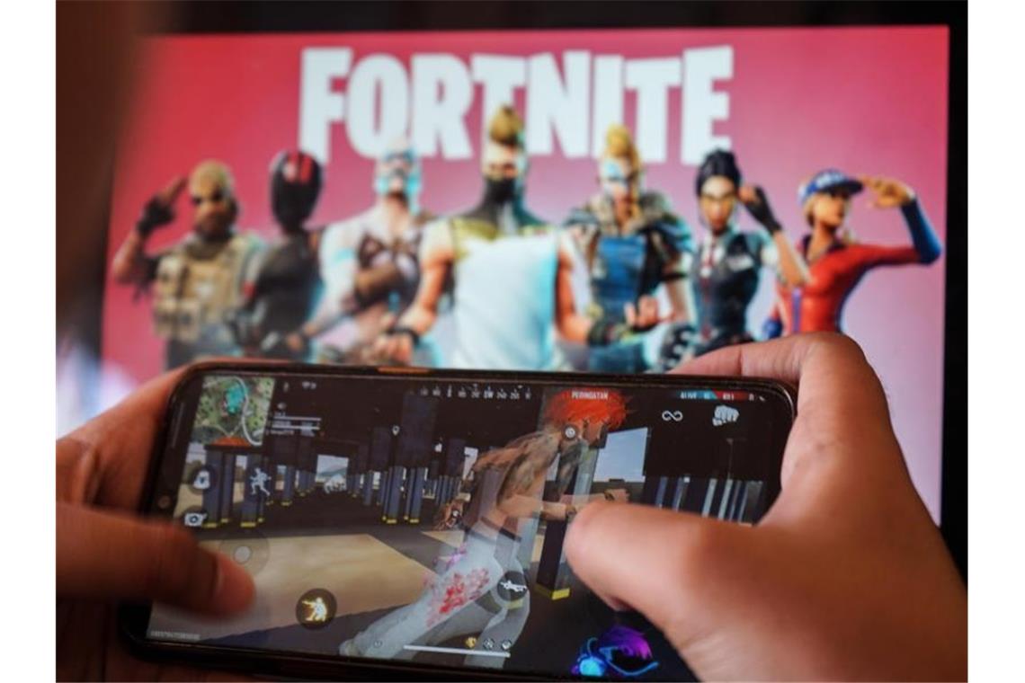 Ein Kind spielt ein Spiel auf einem Mobiltelefon mit einem Bild des Fortnite-Spiels auf dem Computerbildschirm im Hintergrund. (Archivbild). Foto: Herwin Bahar/ZUMA Wire/dpa