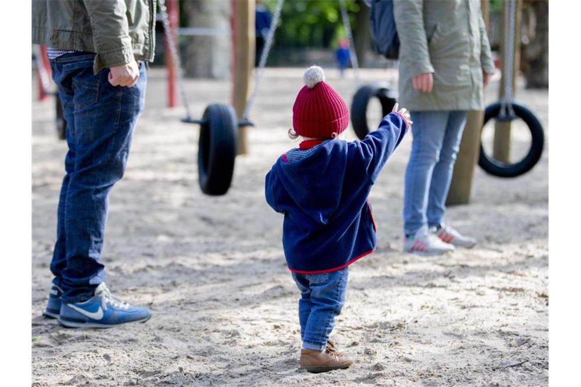 Ein Kind spielt mit seinen Eltern auf einem Spielplatz. Foto: Christoph Soeder/dpa