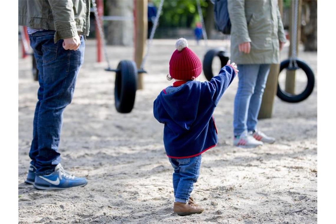 Lohnfortzahlung für Eltern wird wohl nicht verlängert Ein Kind spielt mit seinen Eltern auf einem Spielplatz. Foto: Christoph Soeder/dpa