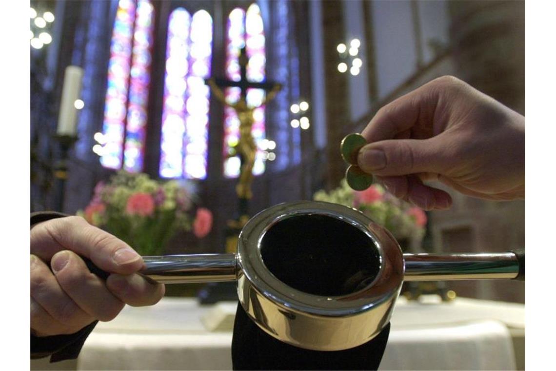 Entfremdung: Immer mehr Menschen treten aus der Kirche aus Ein Kirchenbesucher (r) steckt einige Münzen in einen Klingelbeutel. Foto: Werner Baum