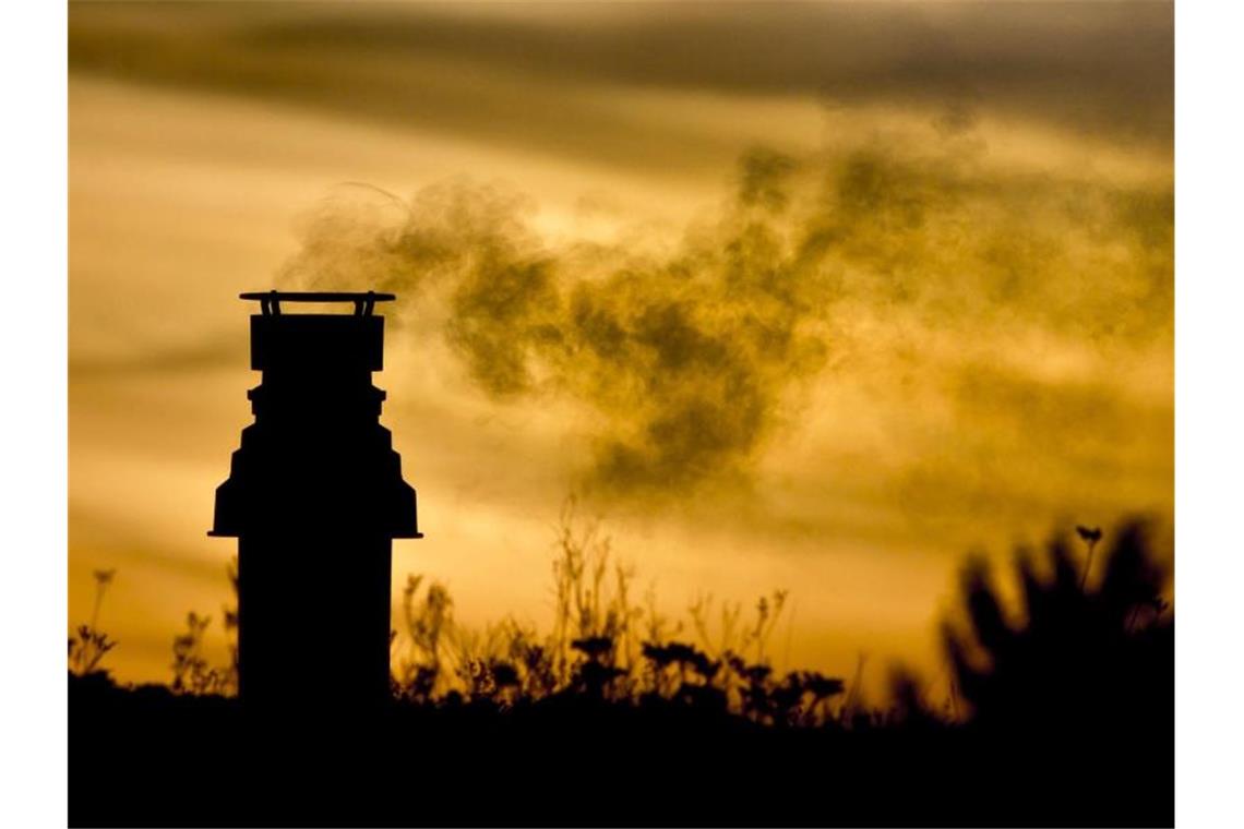 Ein kleiner Schornstein auf einem bepflanzten Dach entlässt bei Sonnenaufgang die Abgase einer Gasheizung in die eiskalte Morgenluft. Foto: picture alliance / dpa