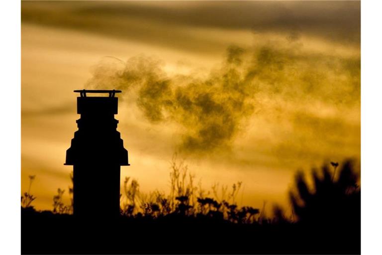 Ein kleiner Schornstein auf einem bepflanzten Dach entlässt bei Sonnenaufgang die Abgase einer Gasheizung in die eiskalte Morgenluft. Foto: picture alliance / dpa