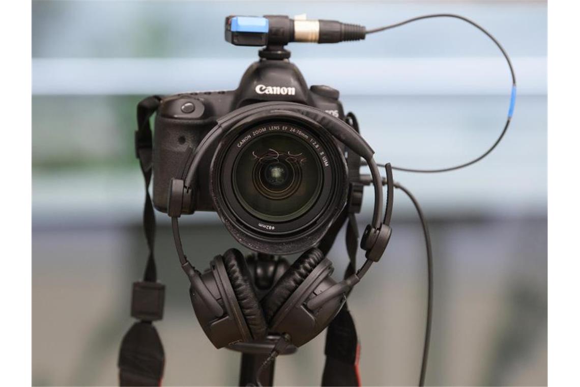 Ein Kopfhörer hängt auf dem Objektiv einer Spiegelreflexkamera. Foto: Robert Michael/dpa-Zentralbild/dpa/Symbolbild