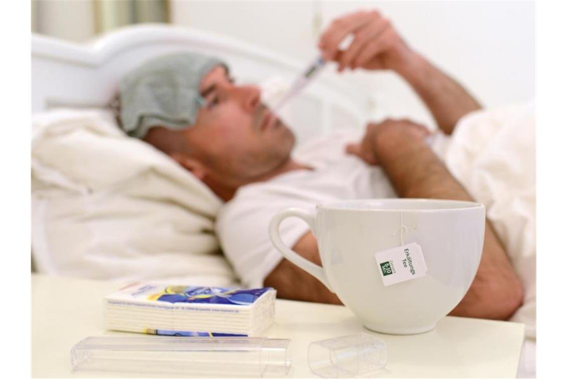 Ein kranker Mann liegt im Bett und misst Fieber. Foto: Andreas Gebert/Archivbild