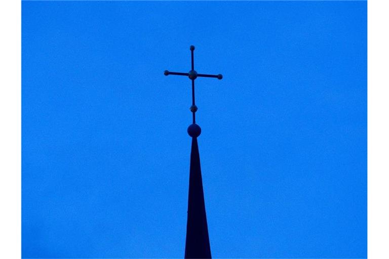 Ein Kreuz auf einem Kirchturm in der Abenddämmerung. Foto: Friso Gentsch/dpa/Symbolbild