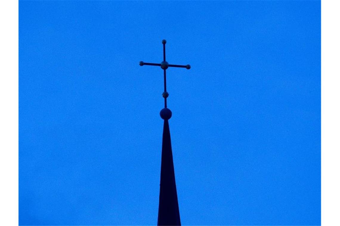 Ein Kreuz ist auf einer Kirchturmspitze zu sehen. Foto: Friso Gentsch/dpa/Symbolbild