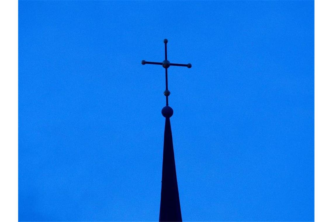 Ein Kreuz ist auf einer Kirchturmspitze zu sehen. Foto: Friso Gentsch/dpa/Symbolbild