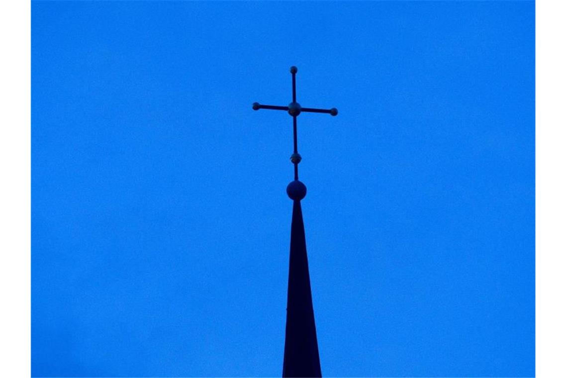 Ein Kreuz sitzt auf einer Kirchturmspitze. Foto: Friso Gentsch/dpa/Archivbild