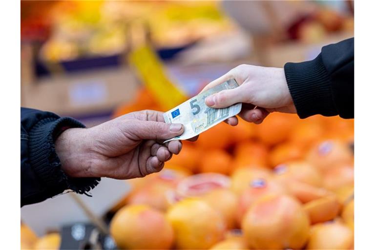 Ein Kunde bezahlt seinen Einkauf an einem Stand auf einem Wochenmarkt mit einem Fünf-Euro-Schein (gestellte Szene). Foto: Moritz Frankenberg/dpa