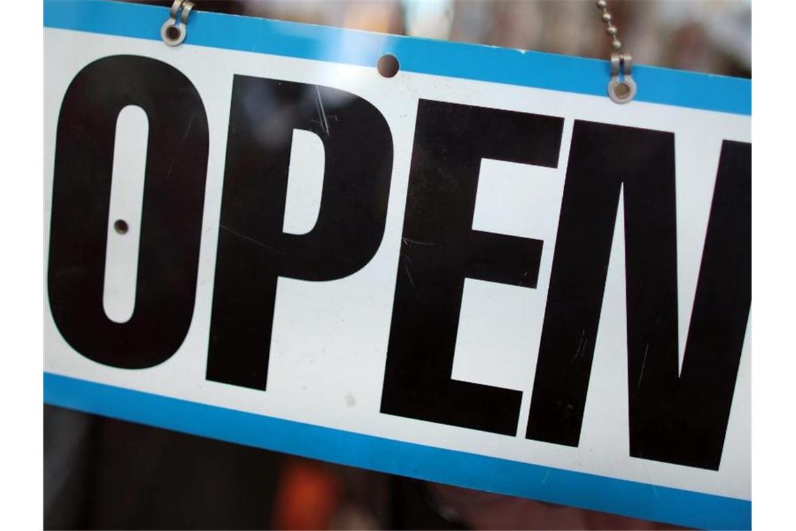 Ein Ladeninhaber dreht an seinem Geschäft das Schild auf „open“ (geöffnet). Foto: Oliver Berg/dpa/Symbolbild