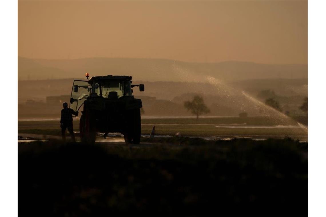 Ein Landwirt steigt neben einem Feld, das bewässert wird, in seinen Traktor ein. Foto: Marijan Murat/dpa