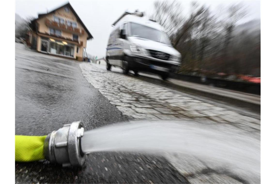 Ein Lieferwagen fährt an einem Feuerwehrschlauch vorbei. Daraus spritzt Wasser, das aus einem überfluteten Keller gepumpt wird. Foto: Patrick Seeger/dpa