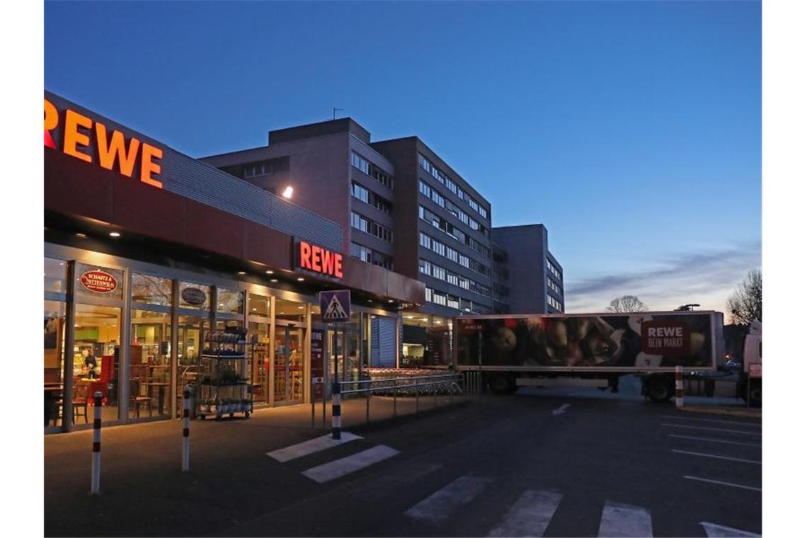Ein Lkw steht am frühen Morgen vor einem Rewe Supermarkt, der mit Waren beliefert wird. Foto: Oliver Berg/dpa