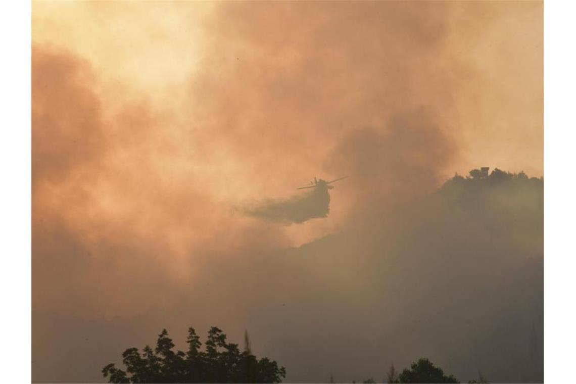 Ein Löschflugzeug wirft über dem antiken Olympia im Westen Griechenlands Wasser auf einen Waldbrand ab. Foto: Giannis Spyrounis/ilialive.gr/dpa