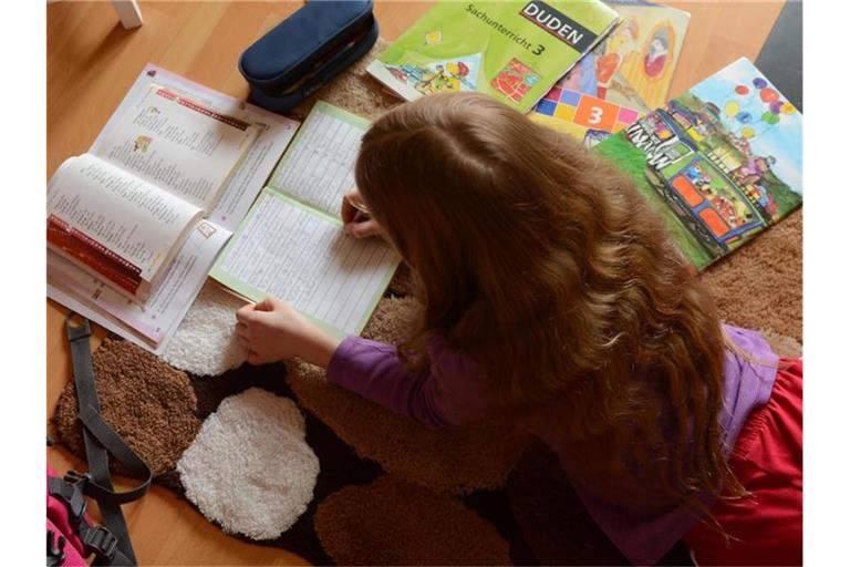 Ein Mädchen liegt auf einem Teppich in seinem Kinderzimmer und erledigt seine Hausaufgaben im Fach Deutsch. Foto: Jens Kalaene/dpa-Zentralbild/dpa