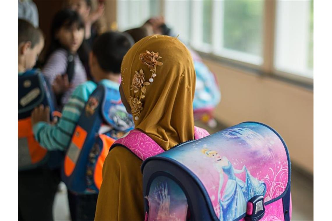 Ein Mädchen mit Kopftuch steht in einer Schule vor einem Klassenzimmer. Foto: Wolfram Kastl/dpa