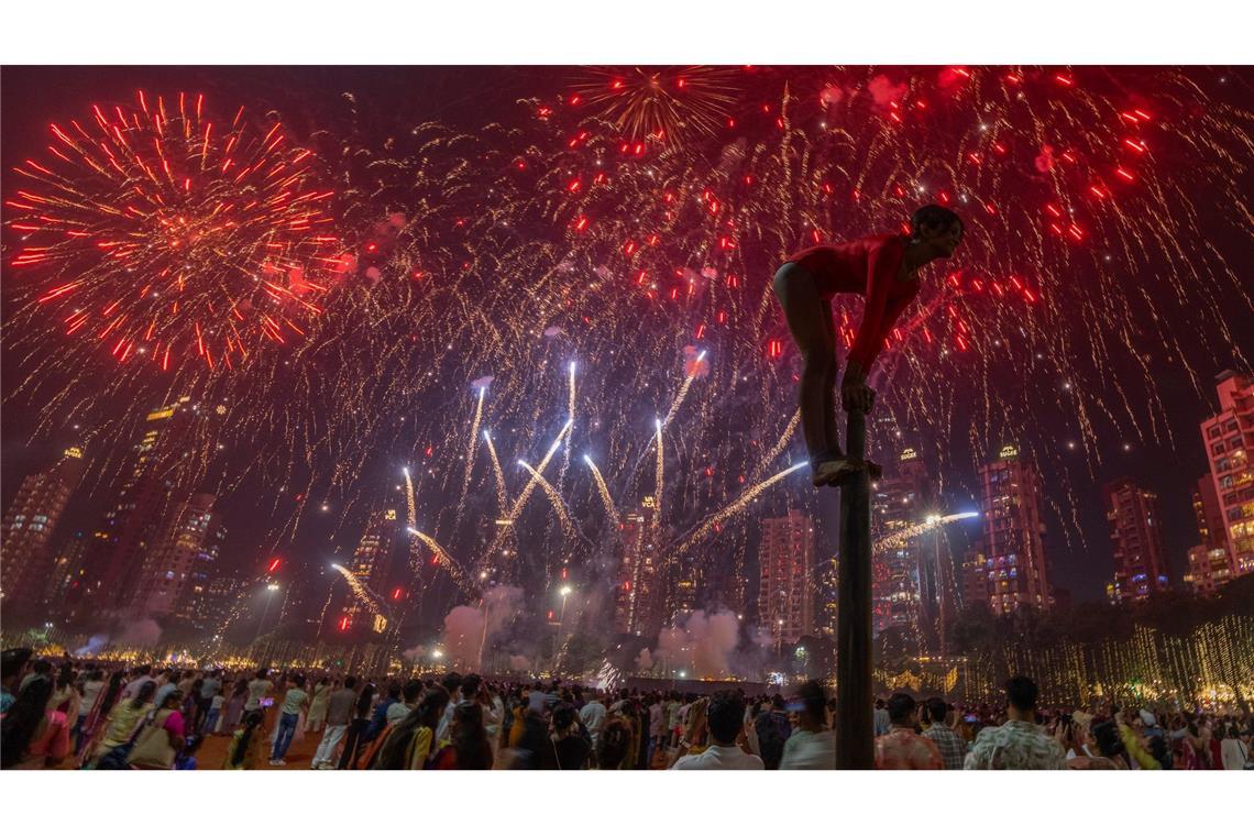 Ein Mädchen performt auf einer Mallakhamb-Stange, während Feuerwerkskörper den Himmel während des Diwali-Lichterfestes in Mumbai erhellen.