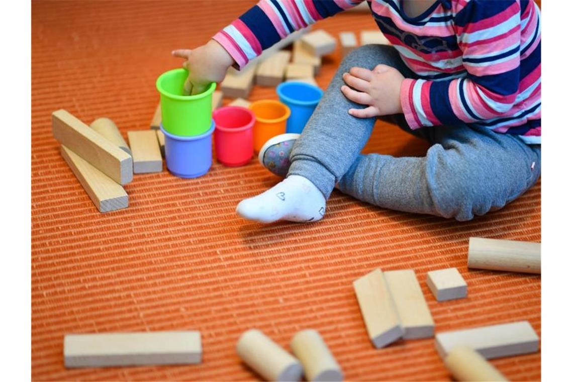 Ein Mädchen spielt in einer Kita mit bunten Bechern und Bauklötzen. Foto: Uwe Anspach/dpa/Symbolbild