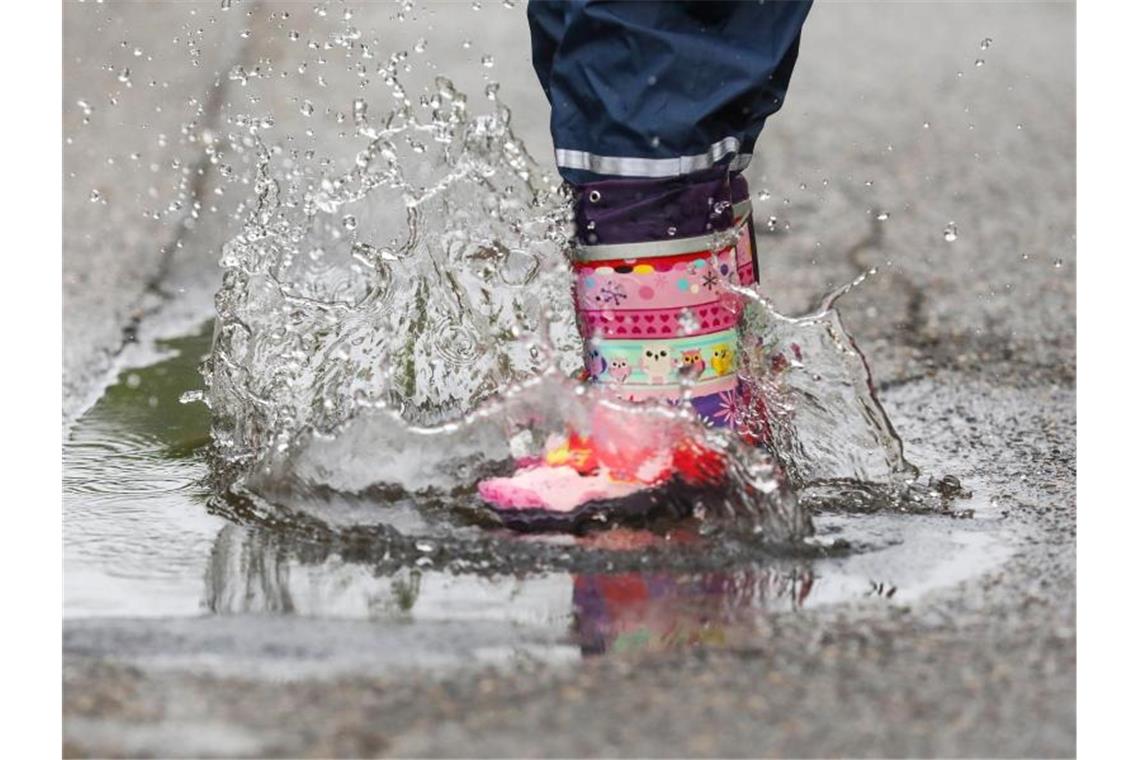 Ein Mädchen springt mit Gummistiefeln in eine Regenpfütze. Foto: Thomas Warnack/dpa/Archivbild