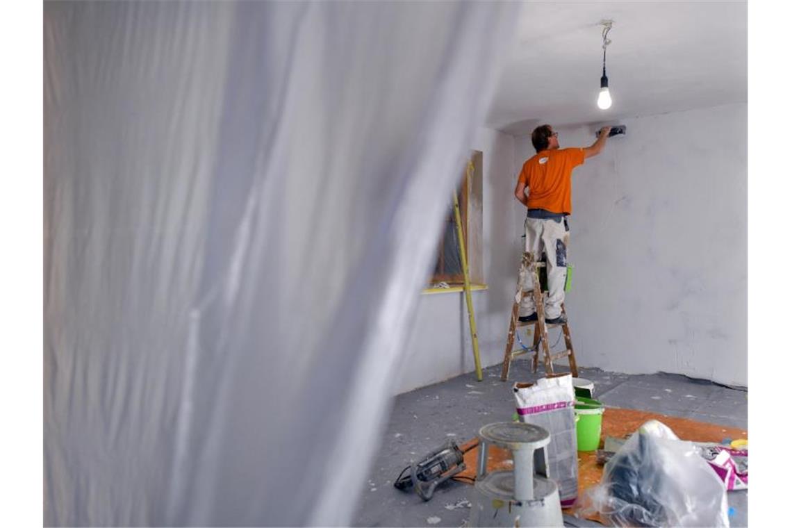Ein Maler spachtelt die Wände eines Zimmers. Foto: Patrick Pleul/Illustration