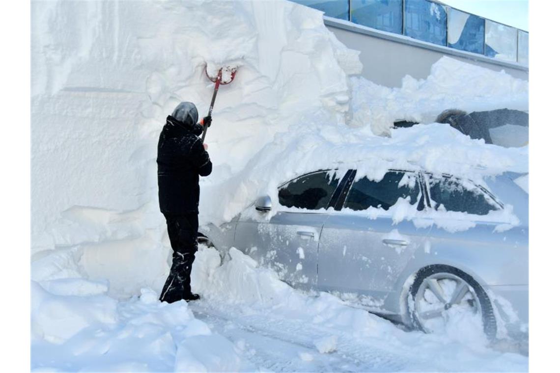 Ein Mann befreit ein eingeschneites Auto von den Schneemengen. Foto: Barbara Gindl/APA/dpa/Symbolbild