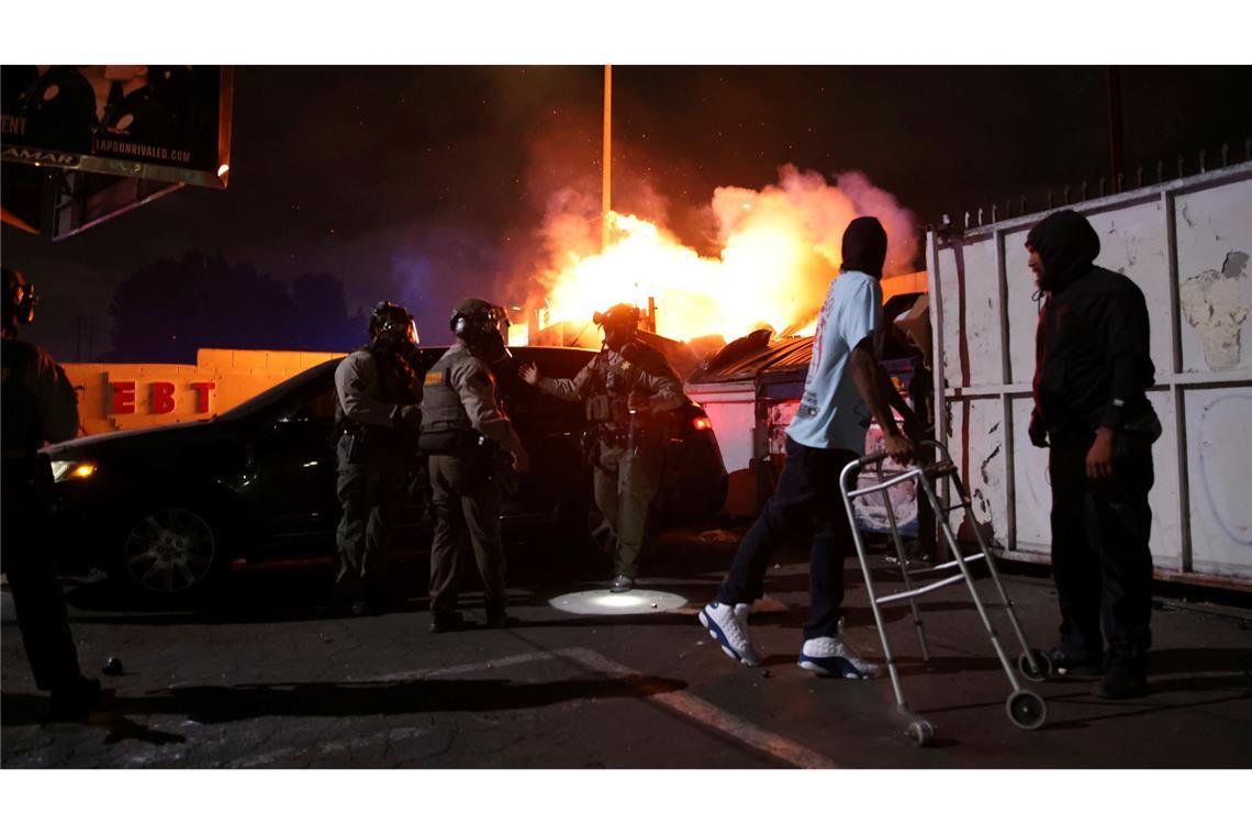 Bilder des Tages Ein Mann blickt auf ein Feuer, nachdem ihm die Strafverfolgungsbehörden während einer Demonstration aus einem Auto geholfen haben. Die Bundeseinwanderungsbehörden haben Operationen durchgeführt.