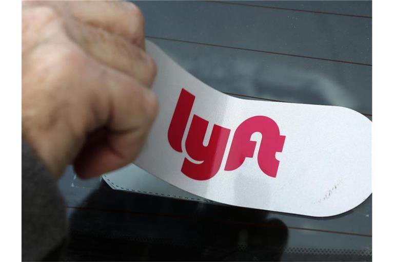 Ein Mann bringt das Logo des Mitfahrdienstes Lyft an einem Auto an. Foto: Gene J. Puskar/AP/dpa