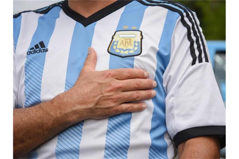 Ein Mann, der ein Trikot der argentinischen Nationalmannschaft trägt, legt sein Hand aufs Herz. (Archivbild). Foto: Julieta Ferrario/dpa