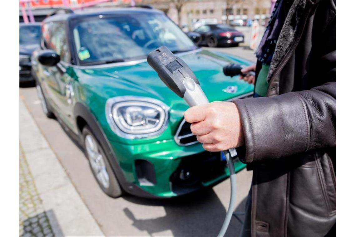 Ein Mann entfernt an einem Auto mit Plug-in-Hybrid-Antrieb in Berlin-Mitte das Ladekabel (Symbol). Foto: Christoph Soeder/dpa