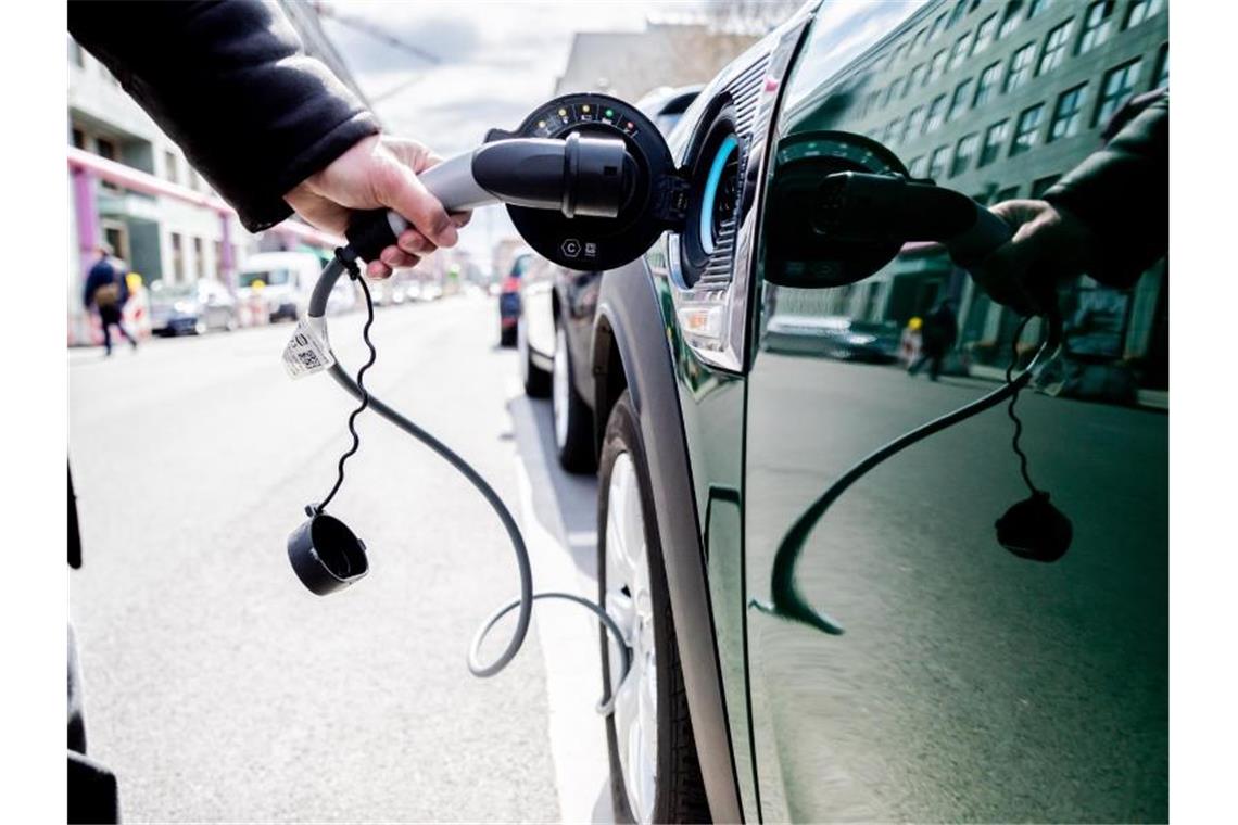 Ein Mann entfernt an einem Auto mit Plug-in-Hybrid-Antrieb in Berlin-Mitte den Stecker. Foto: Christoph Soeder/dpa