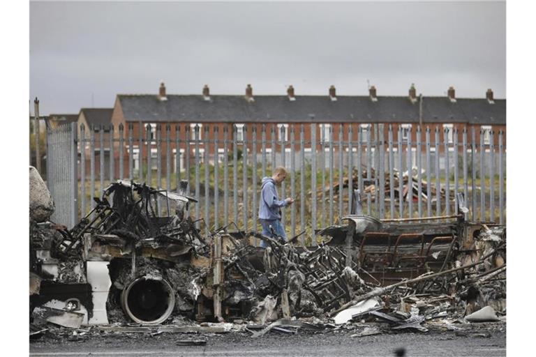 Ein Mann geht an einem ausgebrannten Bus auf der Shankill Road in West Belfast vorbei. Foto: Peter Morrison/AP/dpa