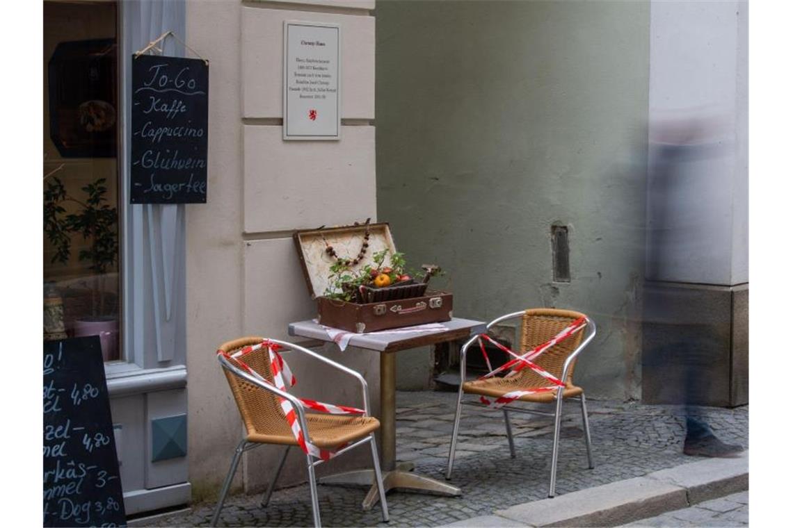 Ein Mann geht an Stühlen eines Cafés vorbei, die mit Flatterband gesperrt wurden. In Passau dürfen die Menschen ihre Wohnung seit Samstag nur noch aus triftigem Grund verlassen. Foto: Lino Mirgeler/dpa