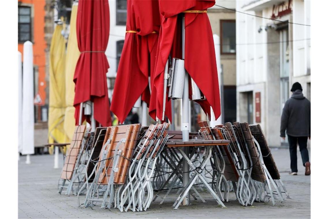 Ein Mann geht auf dem Heumarkt in Köln an zusammengestellten Tischen und Stühlen eines geschlossenen Restaurants vorbei. Foto: Oliver Berg/dpa