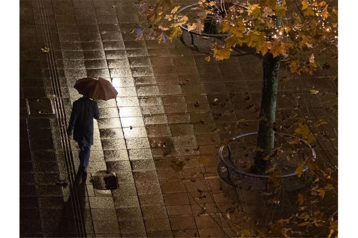Ein Mann geht im Regen an Bäumen vorbei. Foto: Marijan Murat/dpa